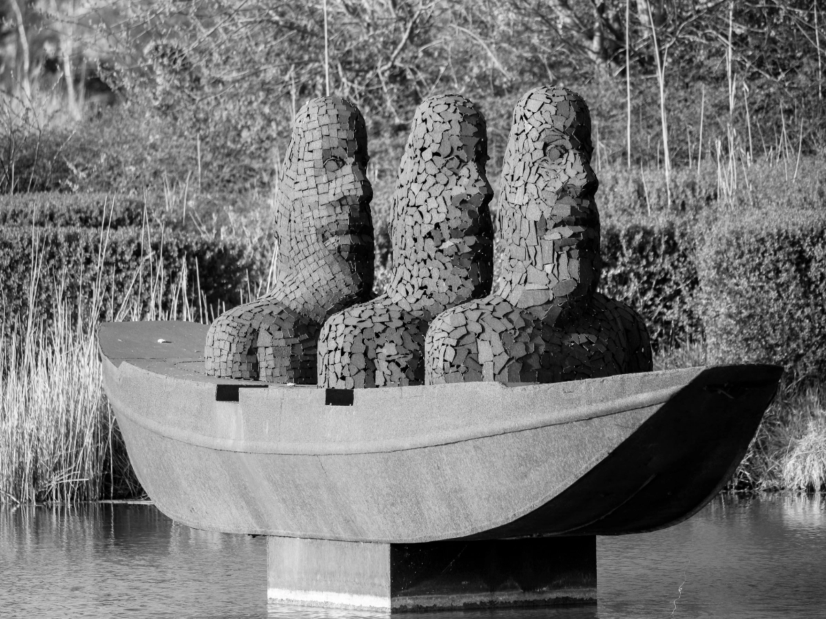 A sculpture of three mosaic-textured figures seated together in a stone boat on water